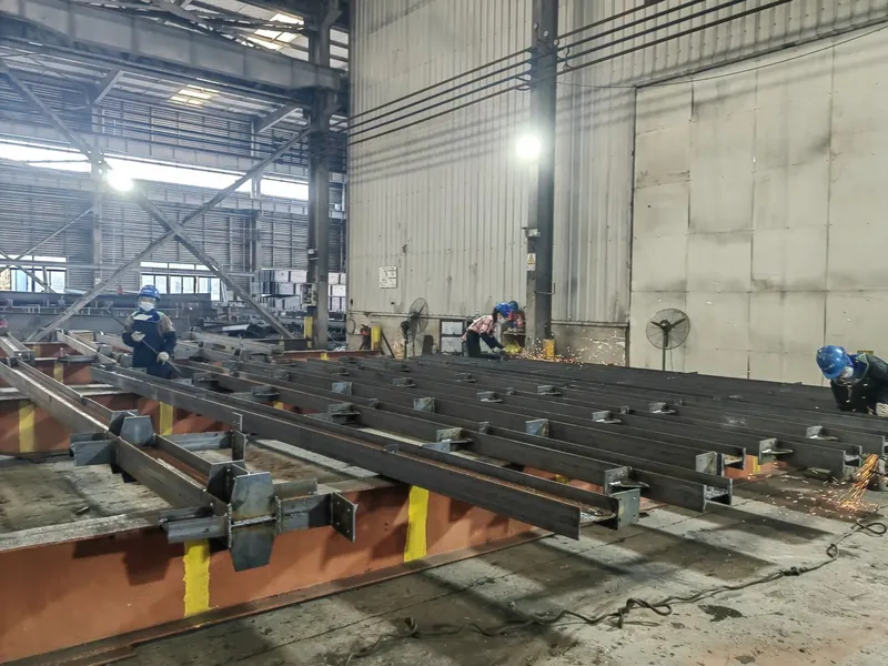 Welders working on steel beams inside the fabrication hall with sparks from CO2 welding