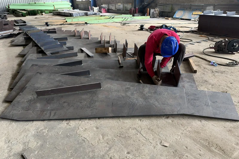 Welder fitting stiffener plates on a steel beam in the fabrication hall