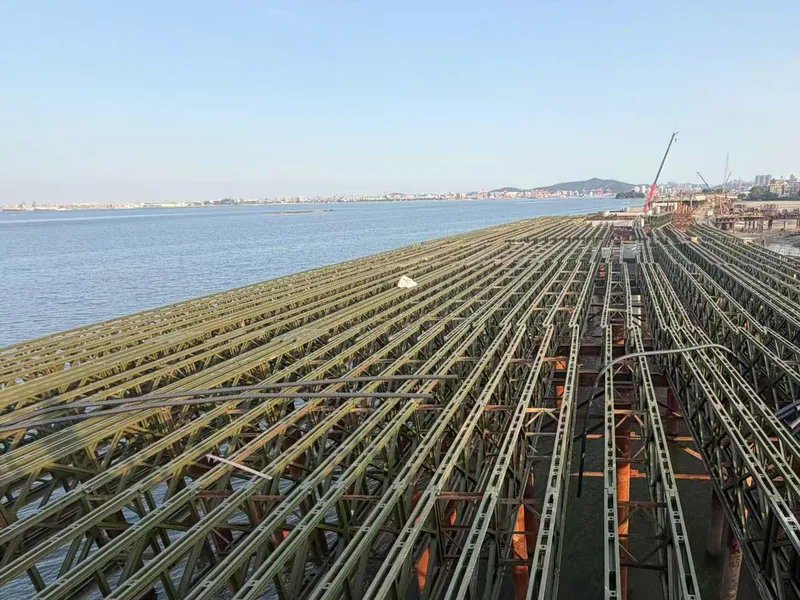 Rows of Bailey trusses forming the working deck over the water, with reinforcement bars laid on top