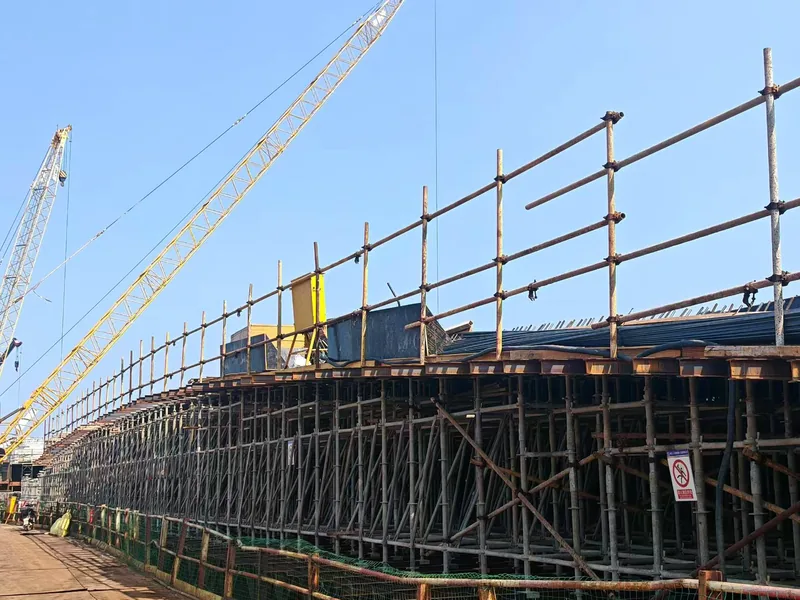 Long run of ringlock falsework under the deck edge, with crawler cranes working alongside