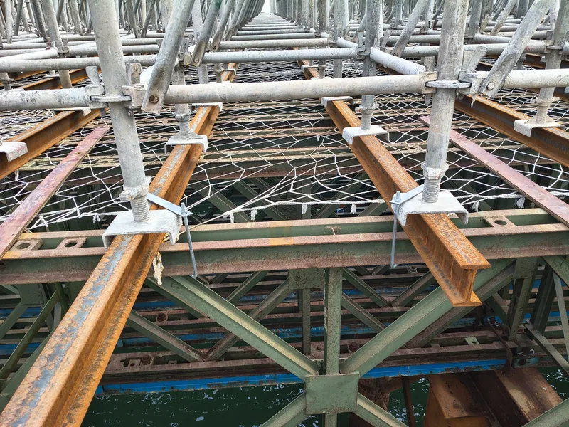 Ringlock standards with adjustable jacks bearing on steel bearers above a green Bailey truss